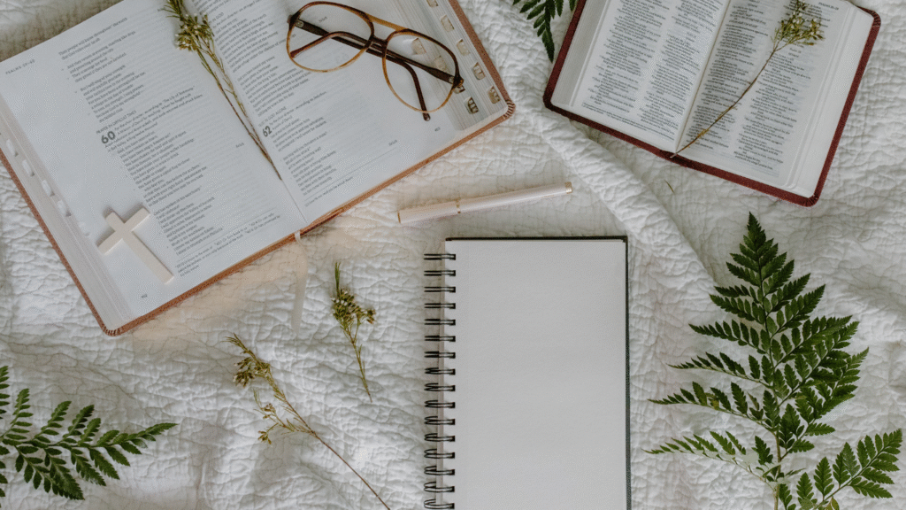 A cozy workspace with open books, glasses, and a blank notebook surrounded by greenery.