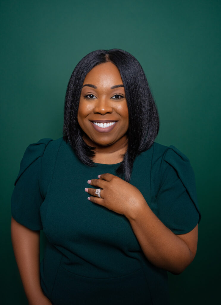 Smiling woman with braided hair in a dark green top.