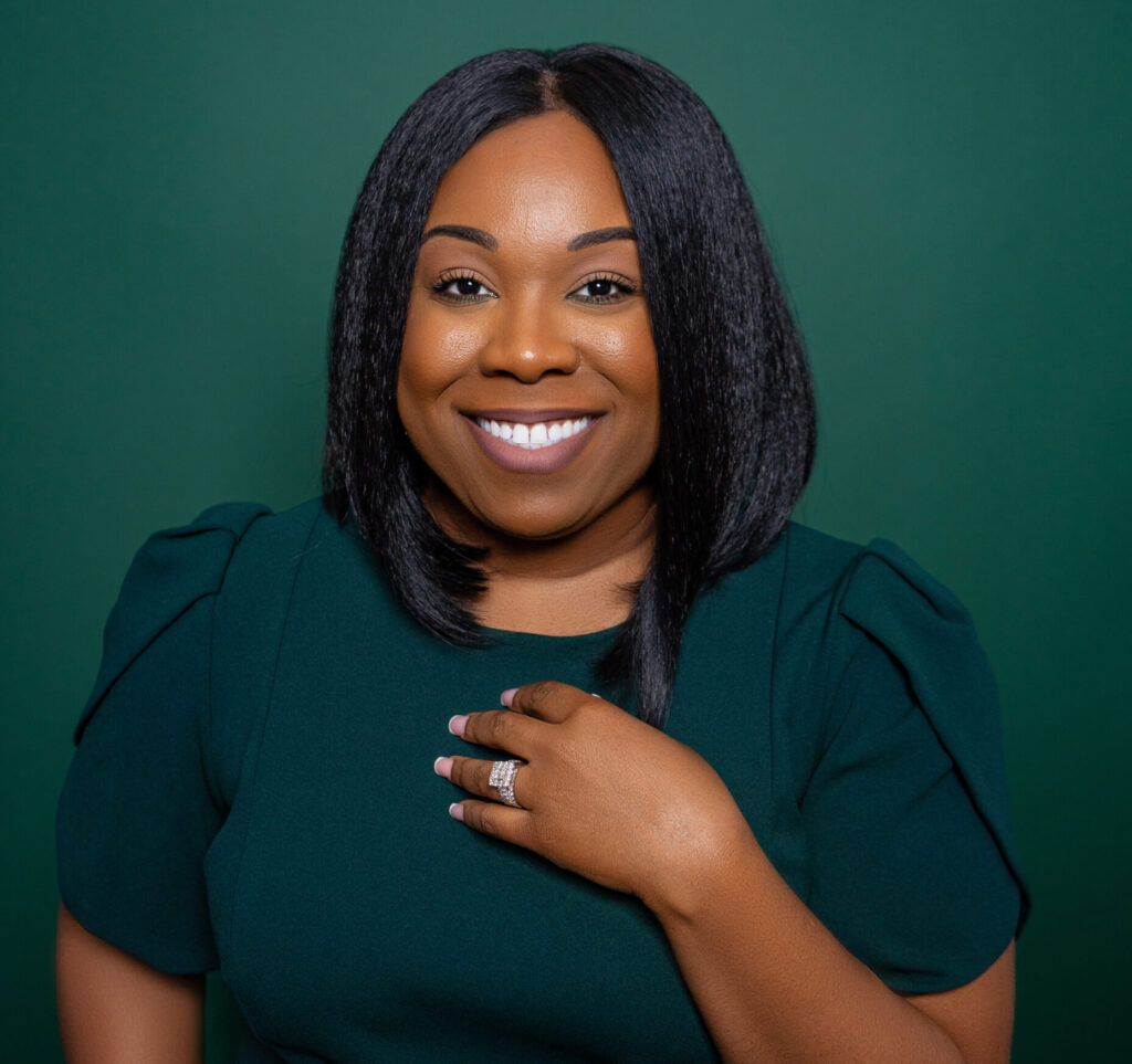 Smiling woman with braided hair in a dark green top against a green background.