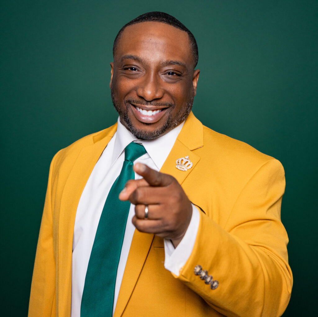 Man in a yellow blazer pointing and smiling confidently.